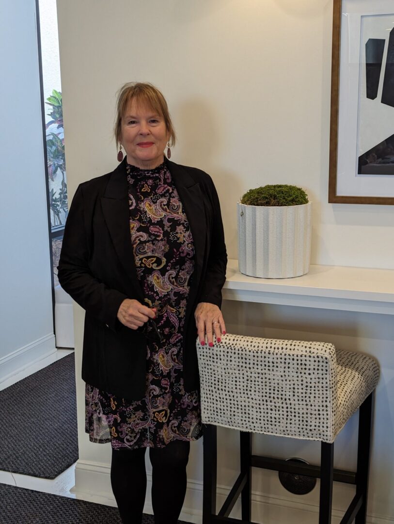 A woman standing next to a chair in front of a wall.